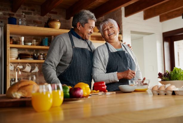 Um casal de idosos sorrindo enquanto cozinham