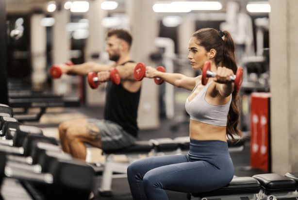 duas pessoas sentadas fazendo elevação lateral